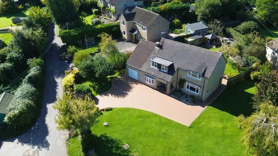 Aerial view of a buff resin bound driveway laid in front of a stone-built detached house with lawn and mature garden.
