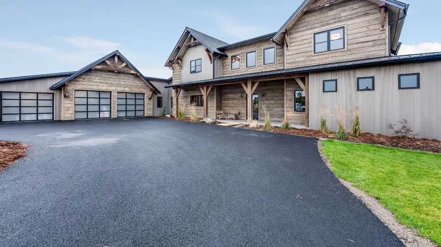 A wide freshly laid tarmac driveway sweeping up to a timber-clad house with a triple garage.